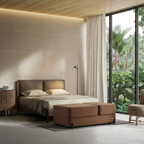 Modern bedroom with brown Ceragem S4 Massage Lounger at the foot of the bed and large window with outdoor view.