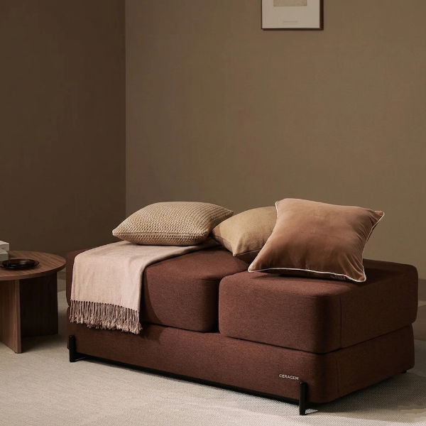 Brown Ceragem S4 massage lounger with pillows and a blanket in a minimalistic room.