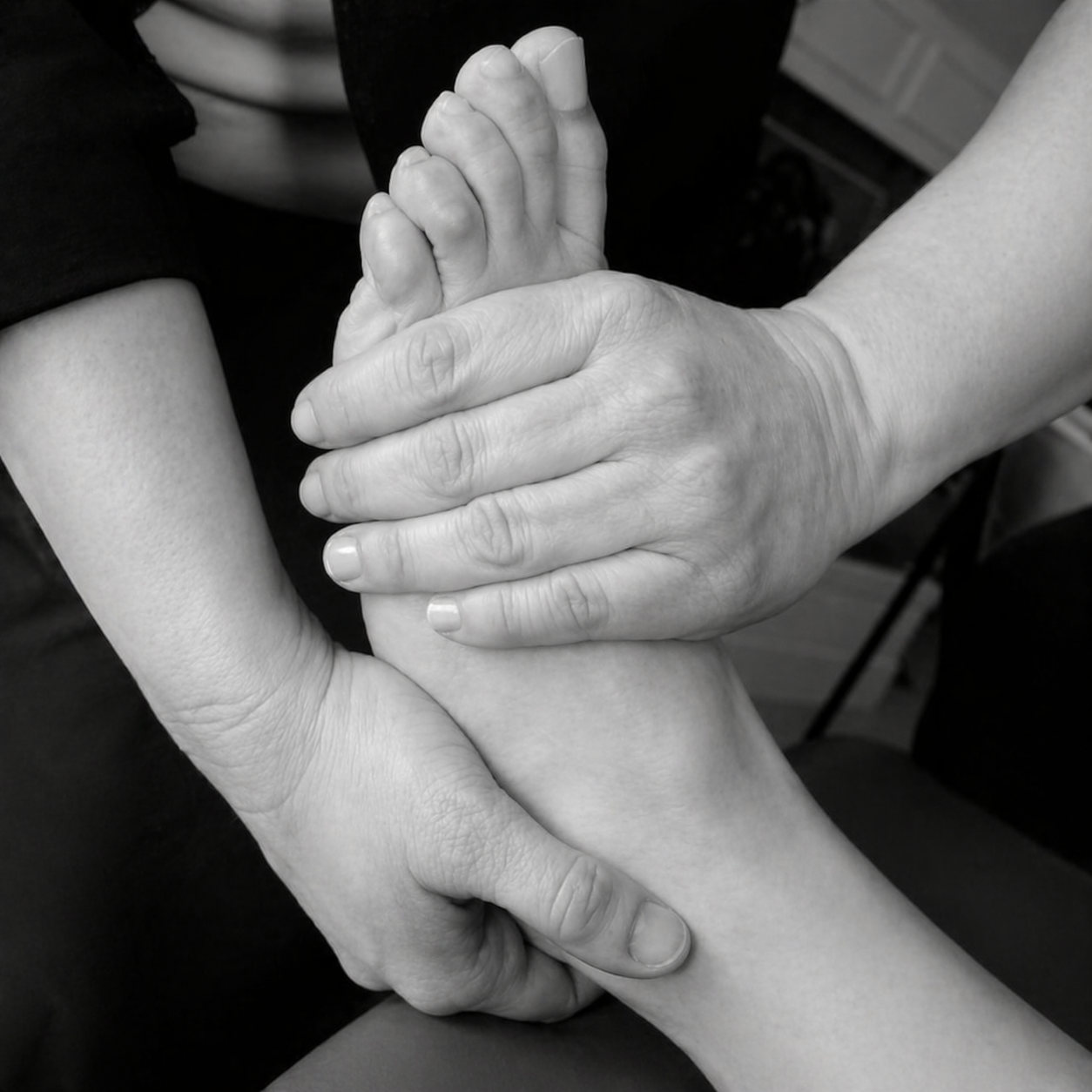 Black-and-white close-up of hands performing a foot massage, focusing on the ankle and sole.